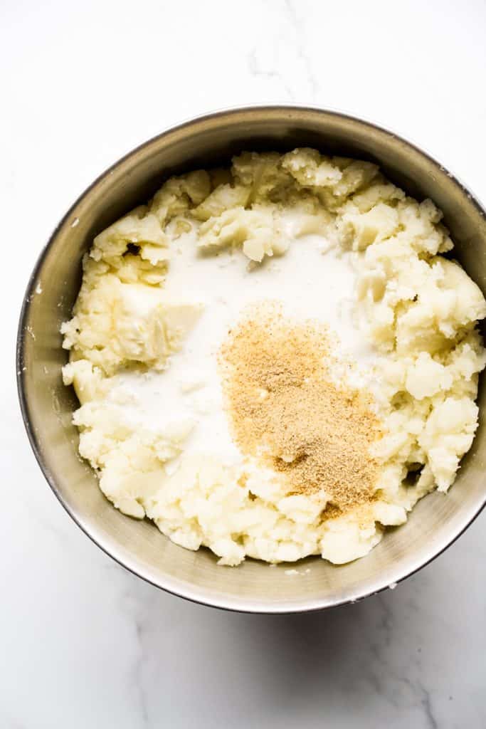 A big bowl of potatoes that are mashed up, along with heavy cream, butter and season salt