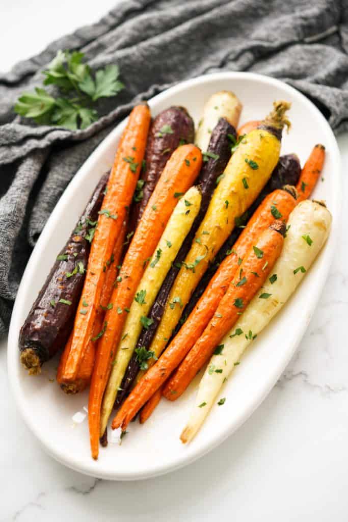 An oval platter filled with whole orange, yellow and purple carrots