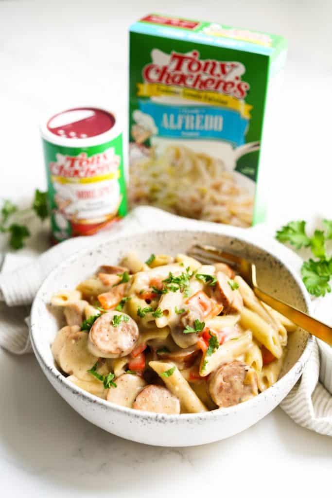 A bowl of cajun sausage pasta with tony chachere's seasonings in the background