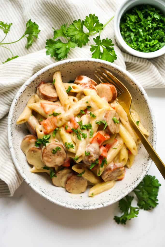 Top down view of a bowl of penne pasta in Cajun alfredo sauce, along with smoked sausage and bell peppers