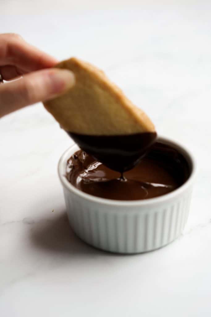 Dipping shortbread cookies into a bowl of melted chocolate