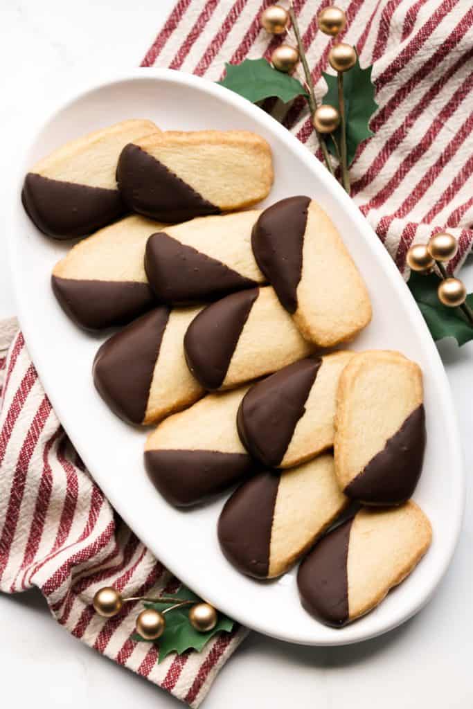 A platter of chocolate dipped shortbread cookies with festive decorations around it