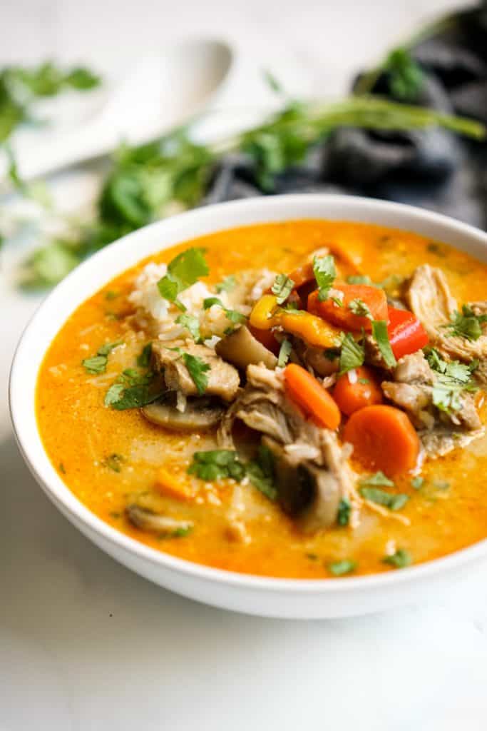 A bowl of coconut curry soup loaded with chicken, rice mushrooms and carrots