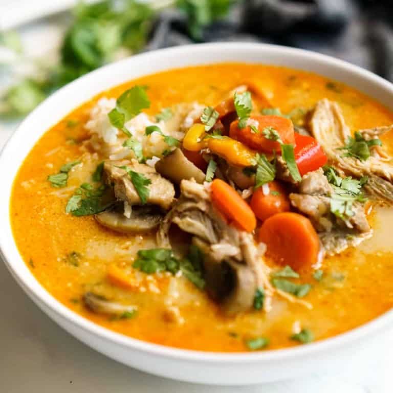 A bowl of thai red curry chicken soup, with cilantro, carrots and mushrooms