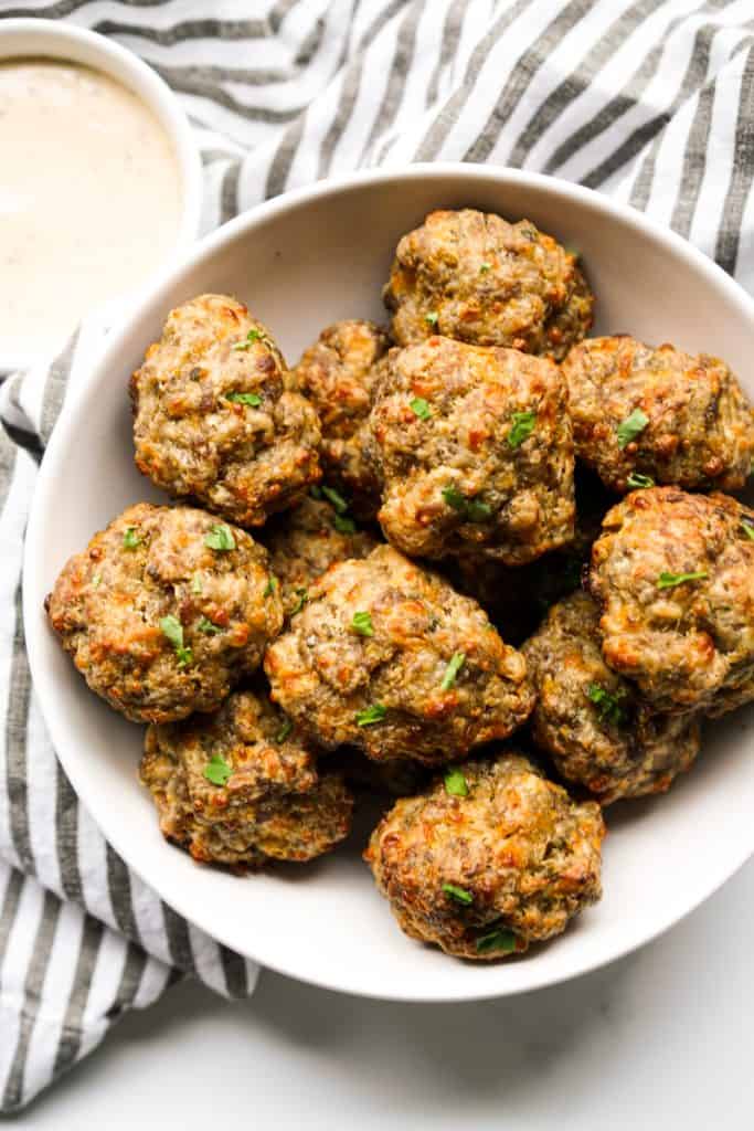 Top down view of a sausage balls in a white bowl, with ranch on the side