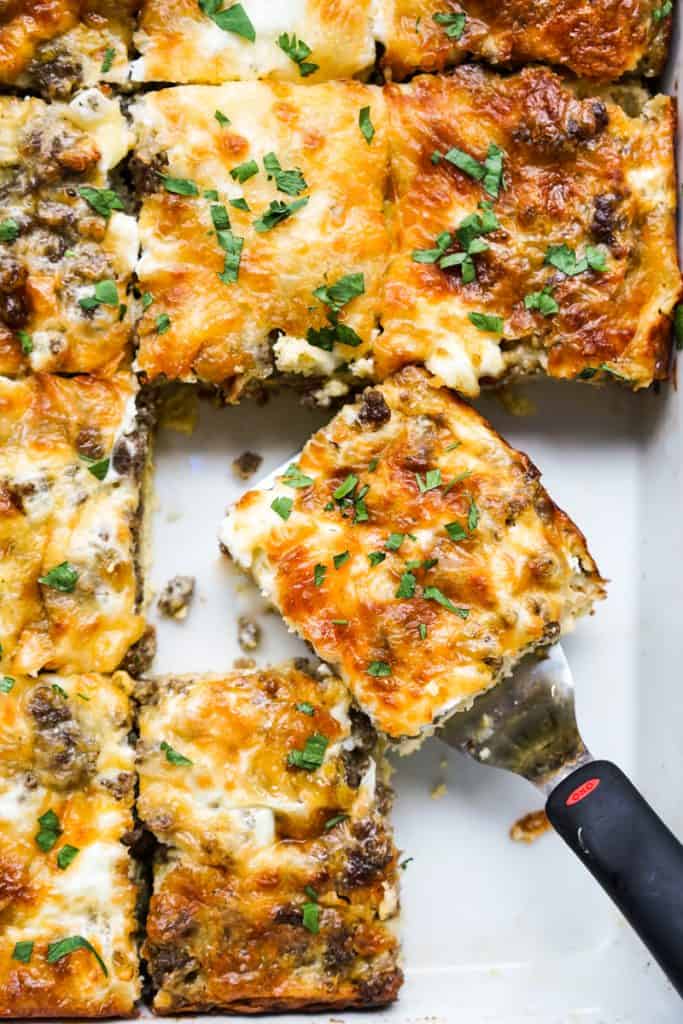 Dishing out one of the square pieces of crescent roll breakfast casserole in a casserole dish