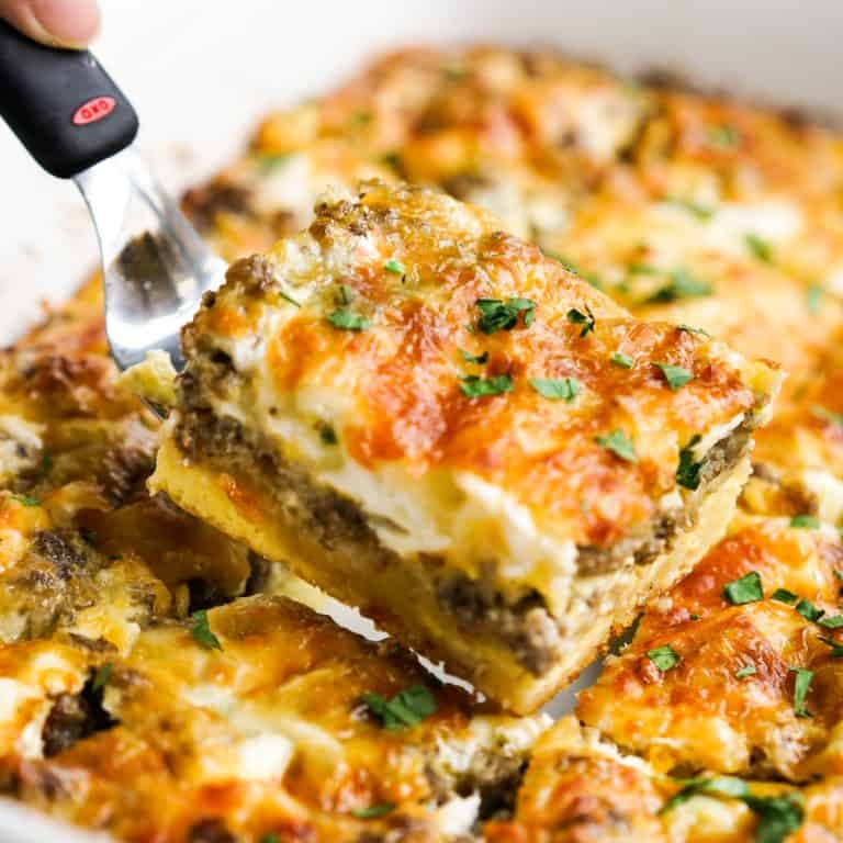 Lifting up a pieces of breakfast casserole with layers of crescent roll, egg, sausage and cheese
