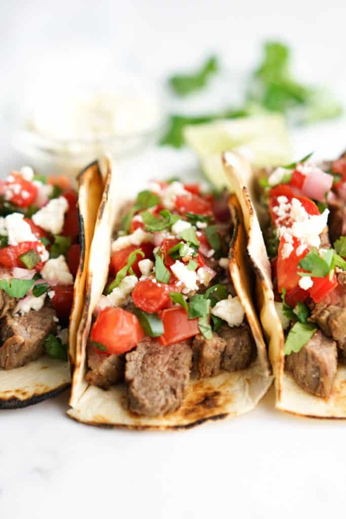 Side view of grilled steak tacos topped with pico
