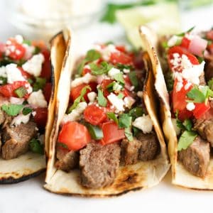 Grilled steak tacos wrapped in frilled tortillas topped with tomatoes, cheese and cilantro