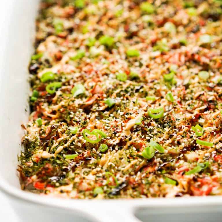 Sushi rice topped with crab mix, sauces and green onions in a casserole dish