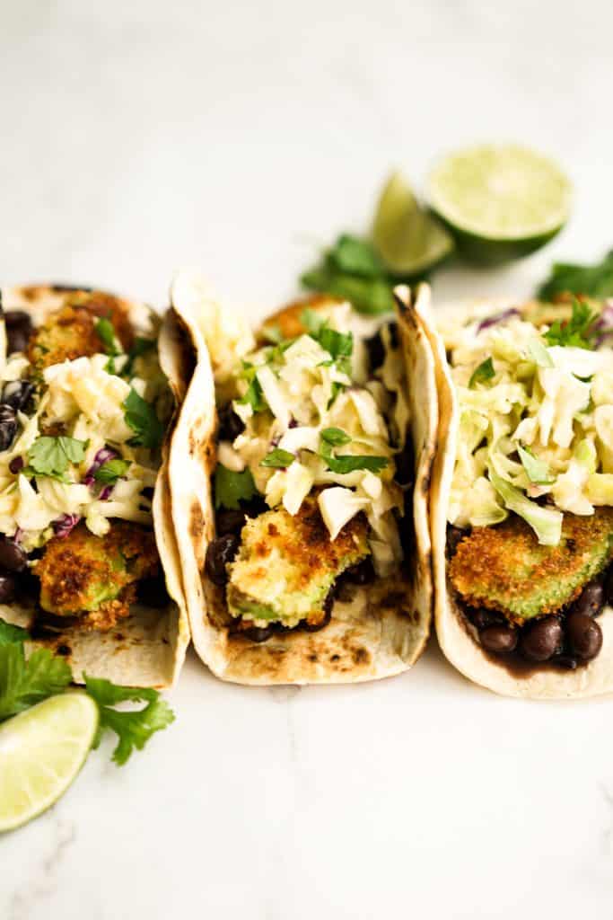 Three fried avocado tacos topped with slaw and combined with black beans at the bottom