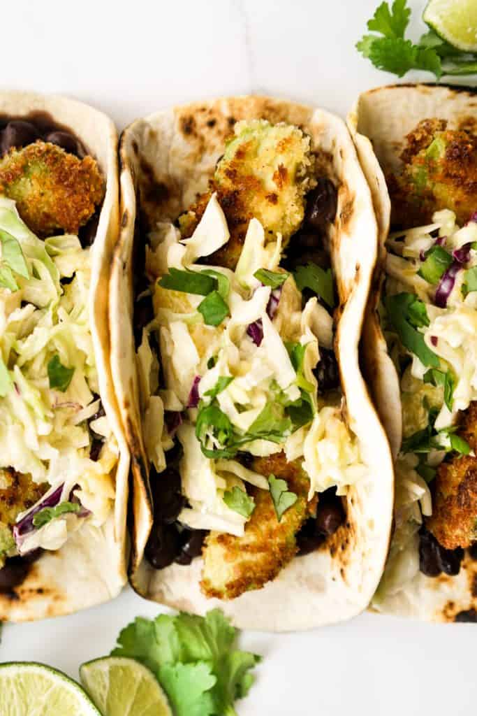 Closeup of fried avocado tacos topped with slaw and cilantro