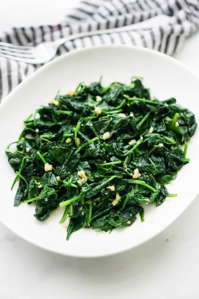 An oval plate of sautéed spinach with fresh garlic