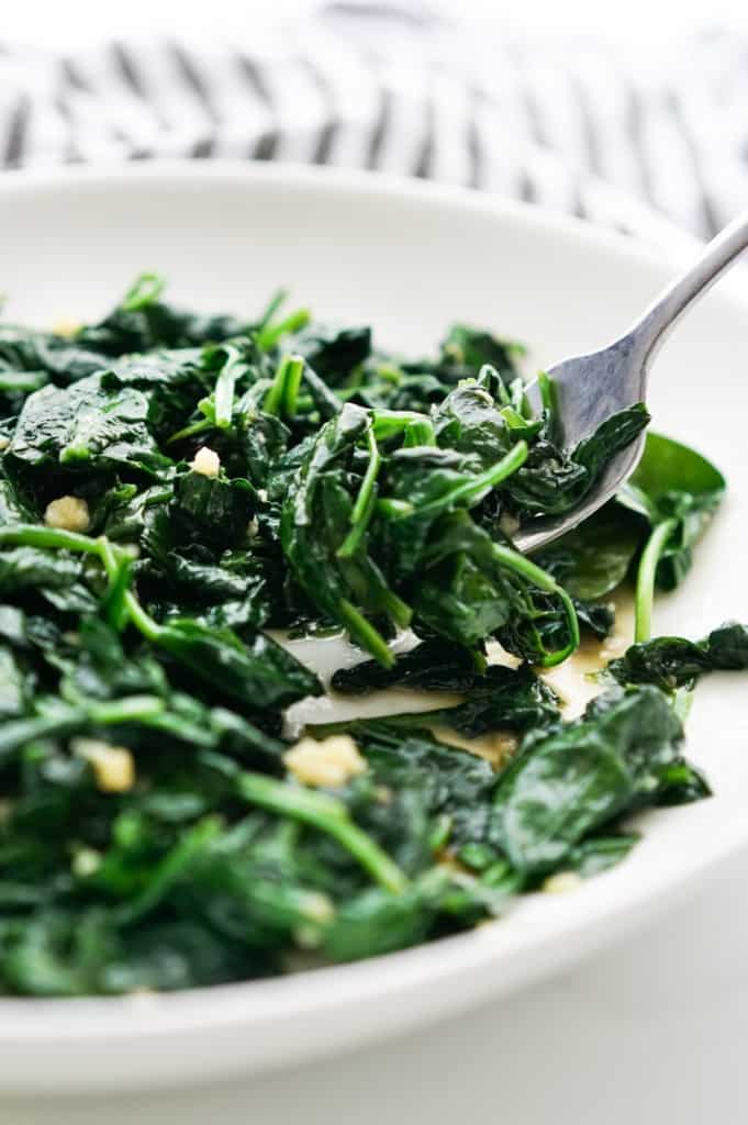 Picking up sautéed spinach from a plate with a fork