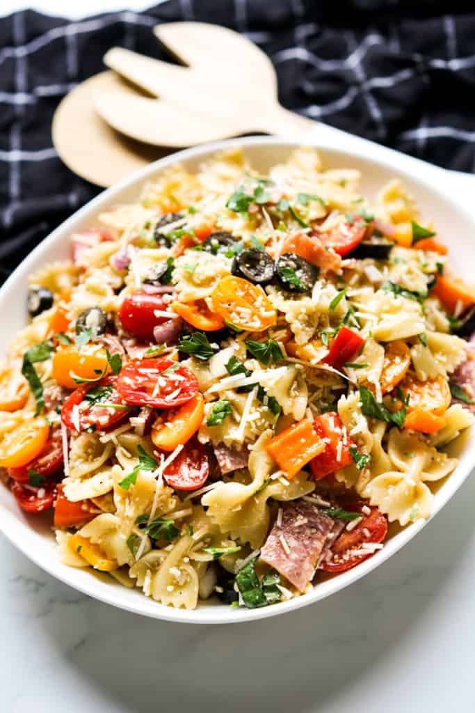 An oval platter of Italian pasta salad with serving utensils in the background