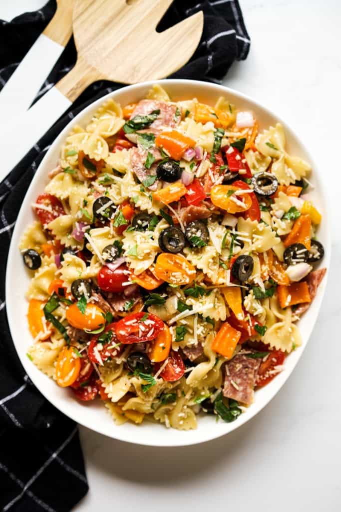 Top down view of an oval bowl, of bow tie pasta salad loaded with tomatoes, red onions, parmesan and fresh basil