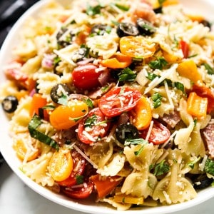 A bowl of bow tie pasta tossed with cherry tomatoes, parmesan, olives, red onions and fresh basil