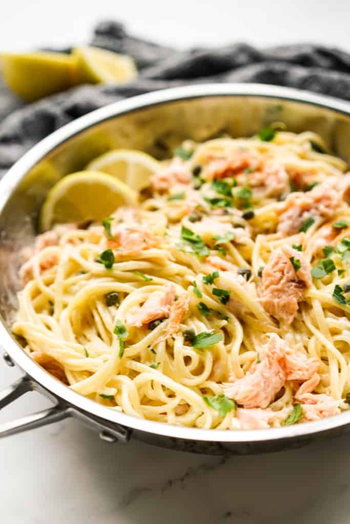 A skillet loaded with smoked salmon pasta tossed in a creamy sauce, along with lemons and capers.