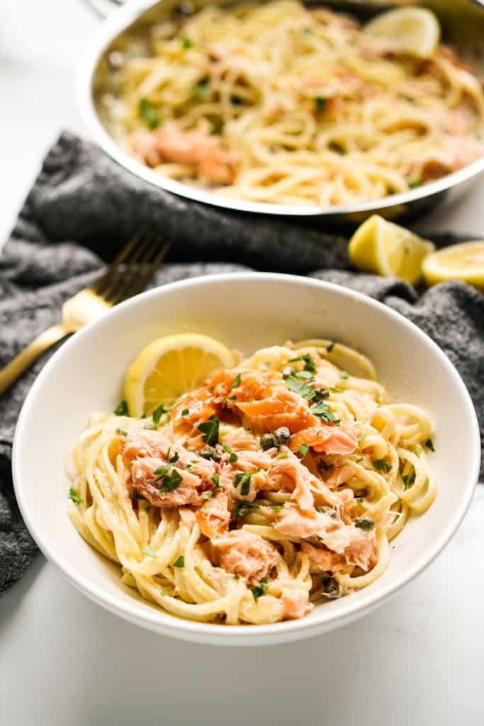 A bowl of smoked salmon pasta with a skillet of it in the background