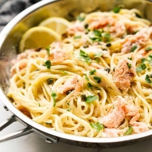 A skillet loaded with creamy smoked salmon pasta, with lemon wedges on the side