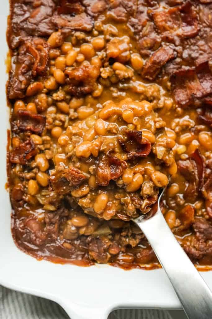 BBQ Baked beans with ground beef and bacon in a casserole dish, scooped out with a serving spoon