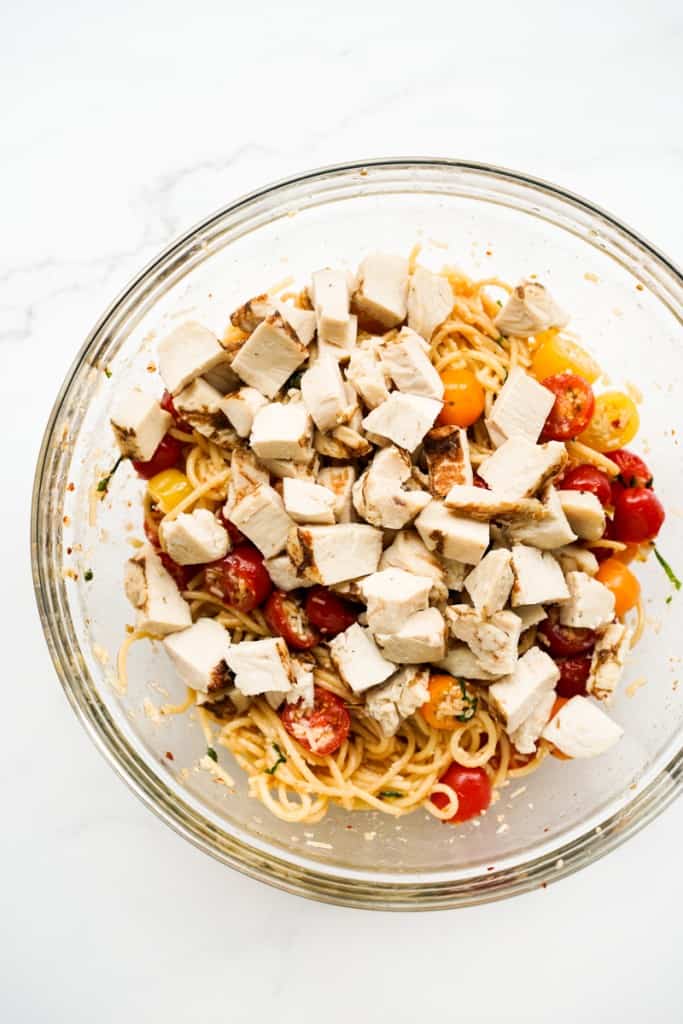 Chicken added to cherry tomato pasta in a mixing bowl