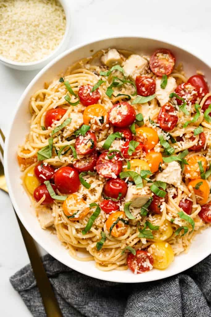 A plate of spaghetti pasta topped with cherry tomatoes, fresh basil, chicken and garlic.