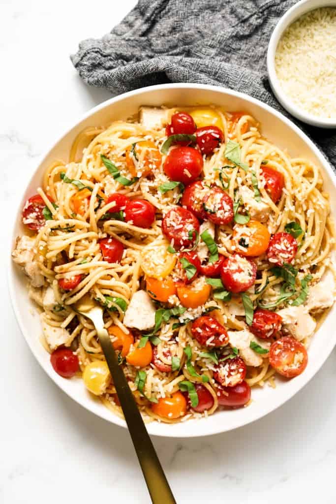 A fork twirling spaghetti in a plate of cherry tomato pasta