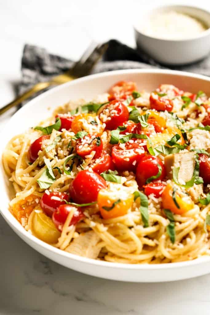 Closeup of a bowl of spaghetti pasta topped with cherry tomatoes, parmesan and basil.