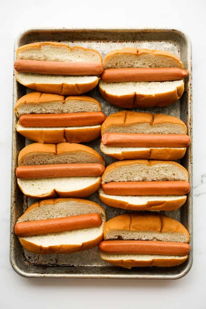 Hot dogs on hot dog buns spread out on a rectangular baking sheet