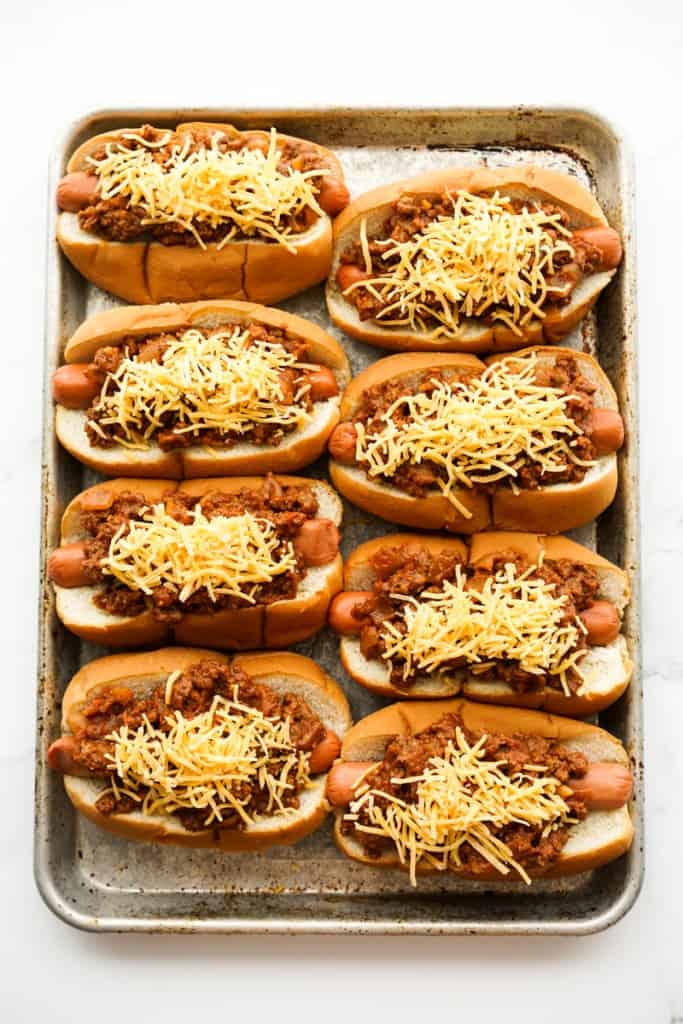 Hot dogs topped with chili and shredded cheese on baking sheet