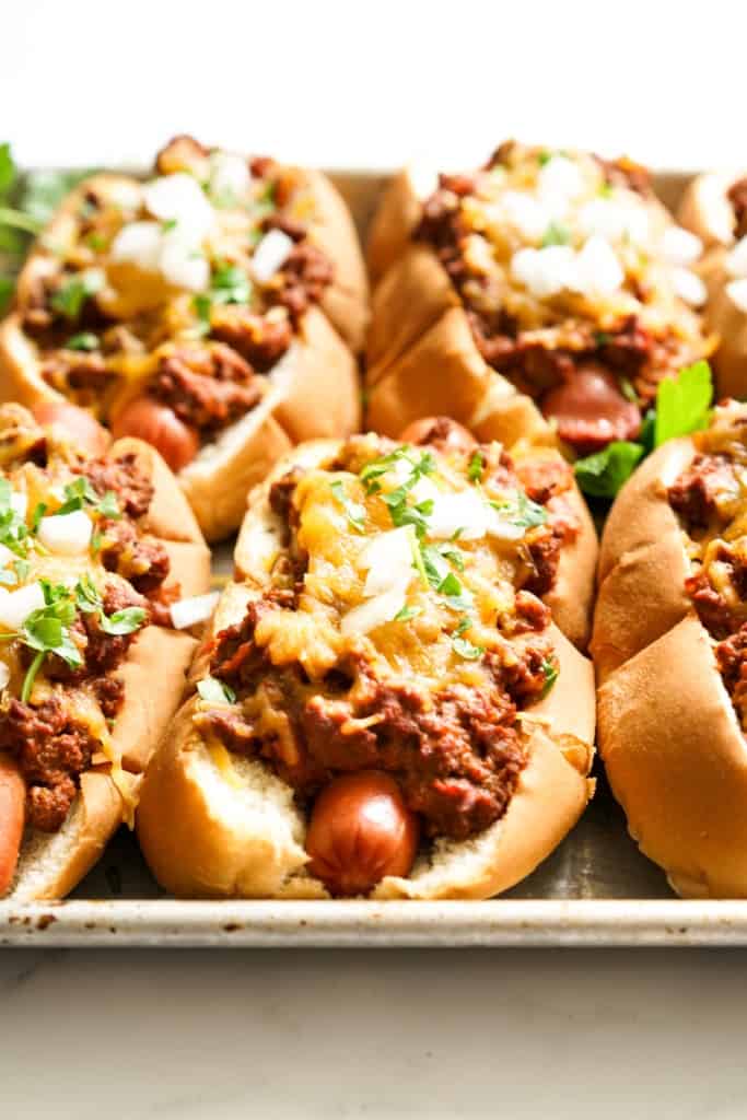 A sheet pan of chili cheese dog topped with cheese, onions and parsley. 
