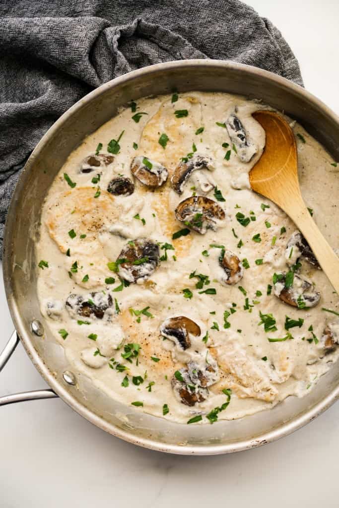 Creamy mushroom chicken with cream sauce in a skillet, wooden spoon on the side