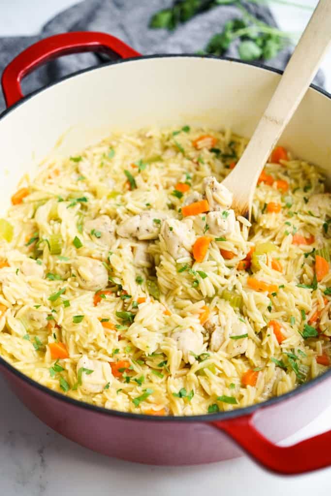 Scooping out chicken and orzo from a pot using a wooden spoon