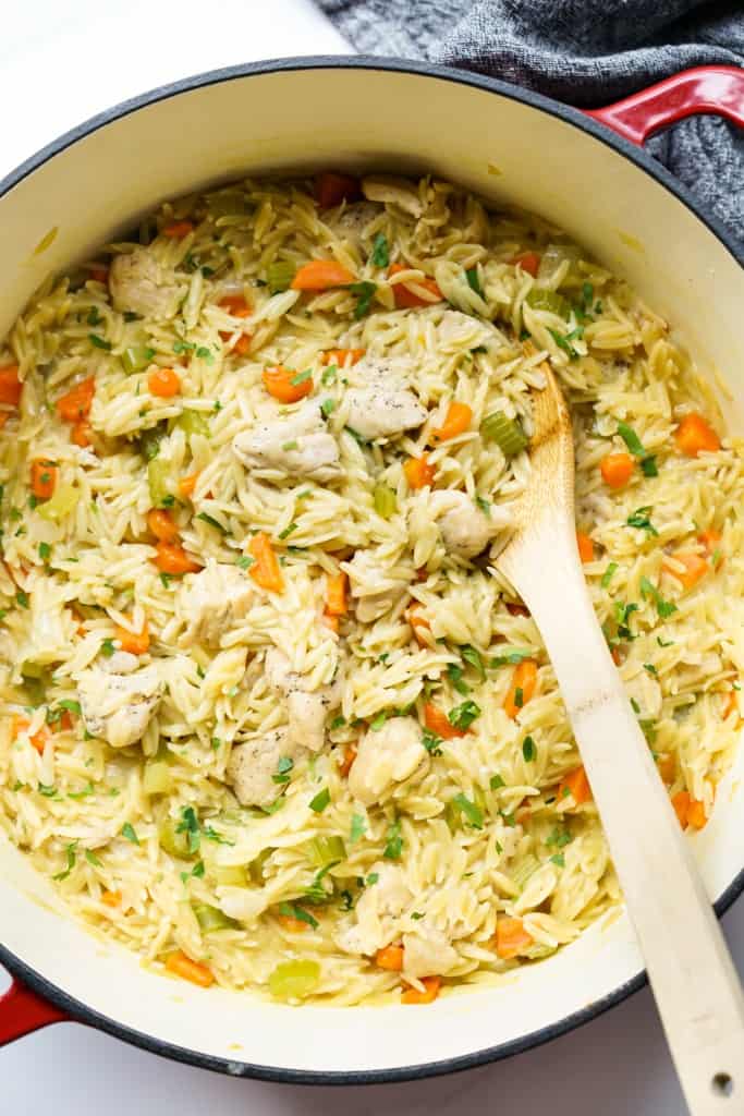 Top down view of chicken and orzo along with diced carrots, celery and onions. Wooden spoon scooping out some of it