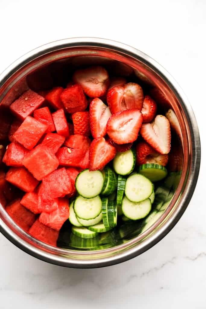 A mixing bowl filled with watermelon chunks, strawberry slices and cucumber slices