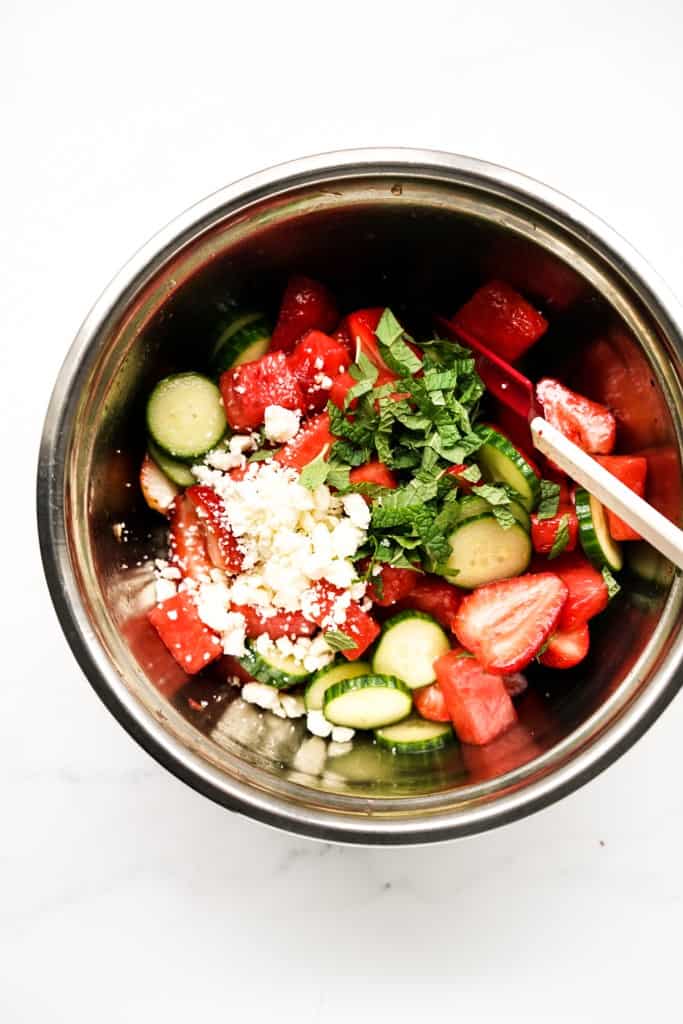 Watermelon strawberry salad topped with mint leaves and feta cheese in mixing bowl