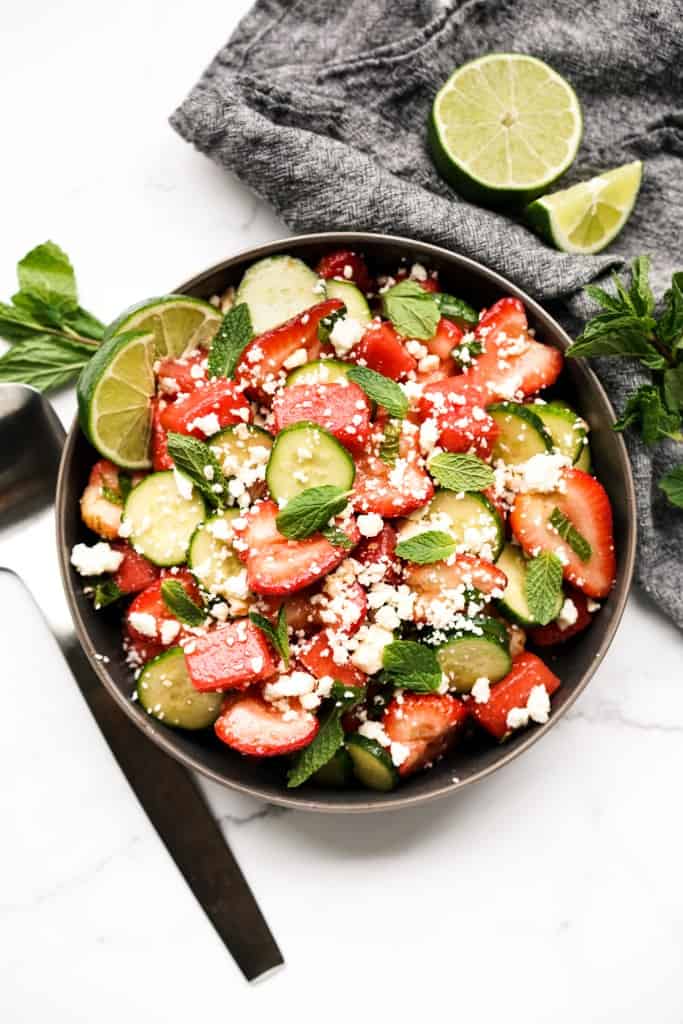 Top down view of a large bowl of watermelon strawberry feta salad, with serving spoon and lime wedges on the side