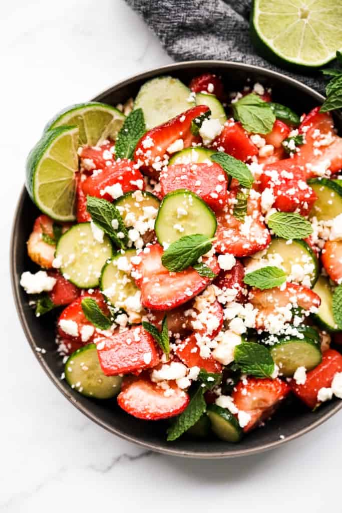 A black bowl of watermelon strawberry salad topped with feta and mint leaves