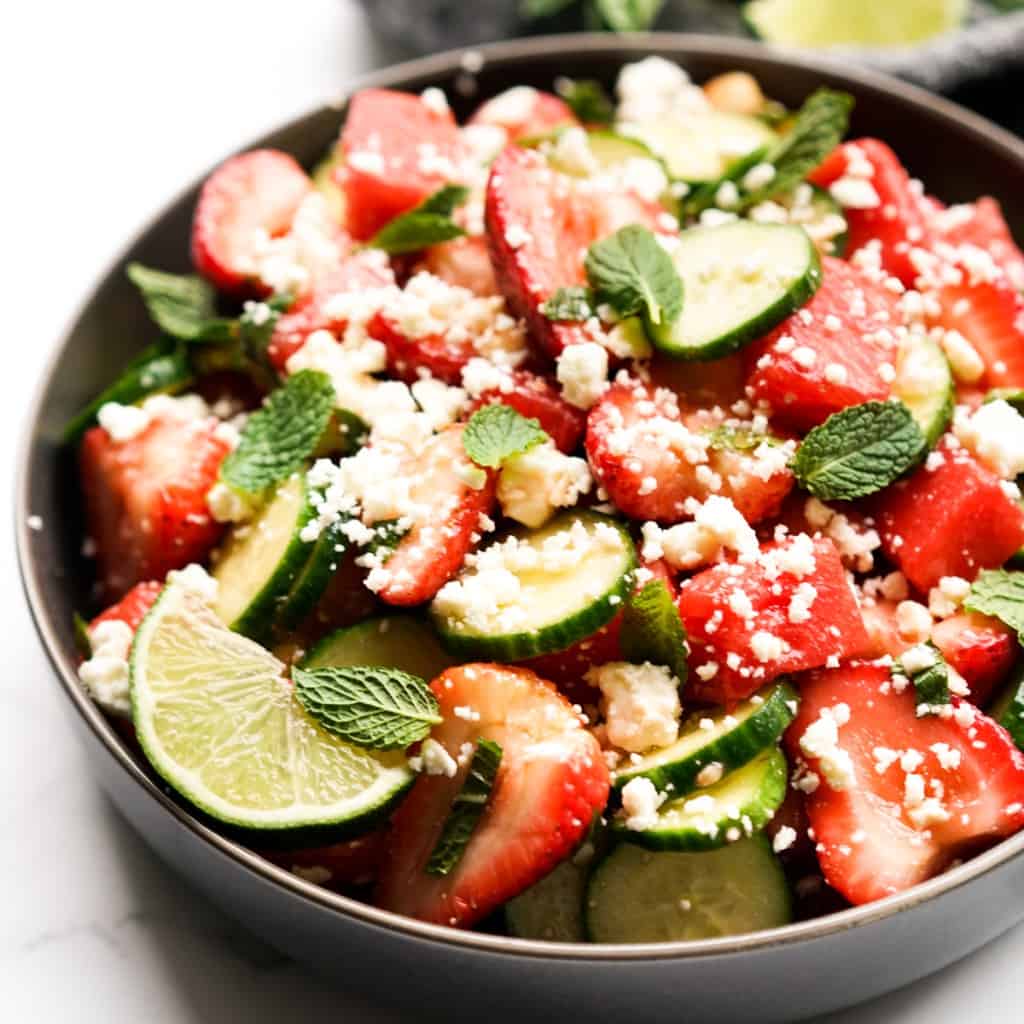 A bowl of watermelon strawberry salad with a wedge on lime