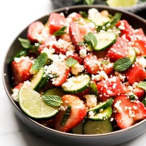 A bowl of watermelon strawberry salad with a wedge on lime