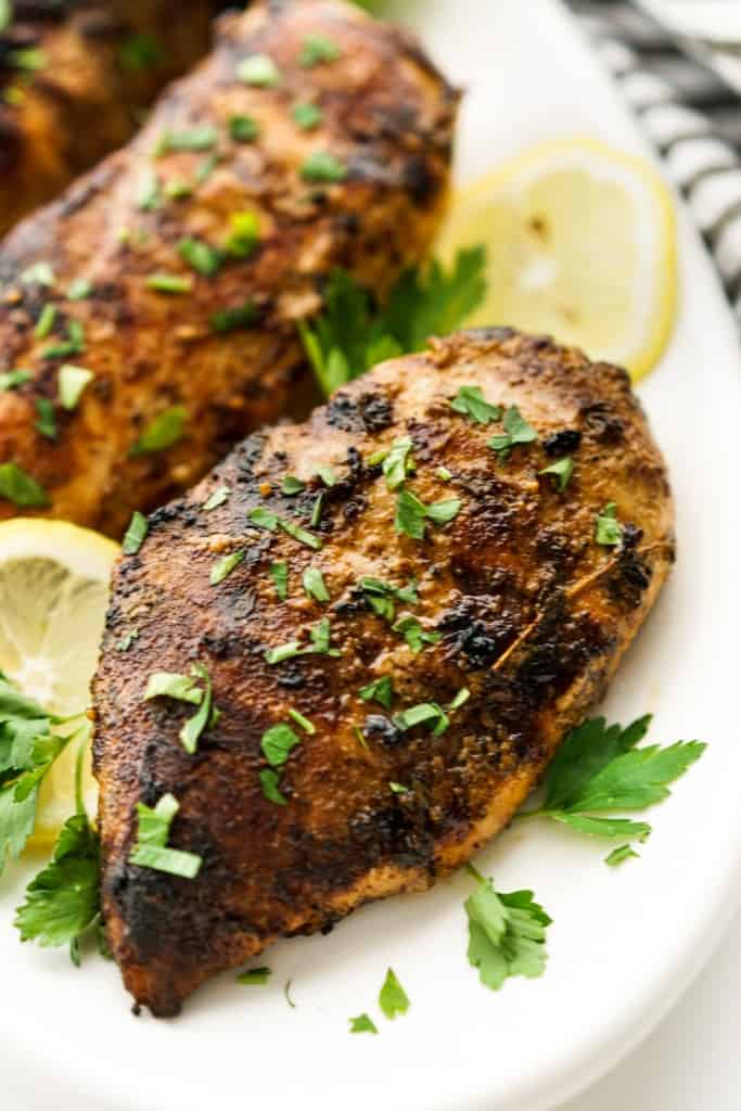 Two large pieces of grilled Italian chicken breast on a plate topped with parsley