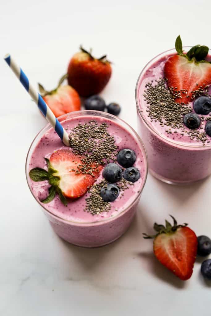 Smoothie topped with sliced strawberries, blueberries, chia seeds and a straw in it