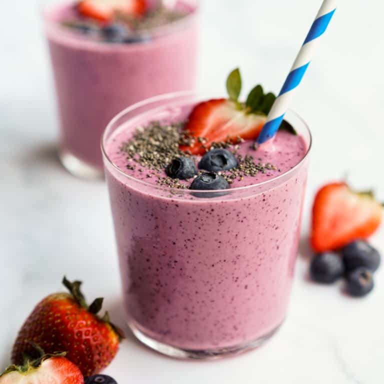 Two glasses of smoothie topped with sliced strawberries, blueberries and chia seeds