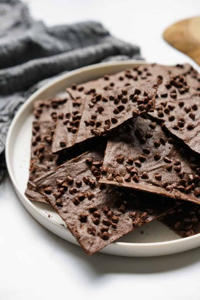 A round plate stacked full of brownie brittle topped with mini chocolate chips