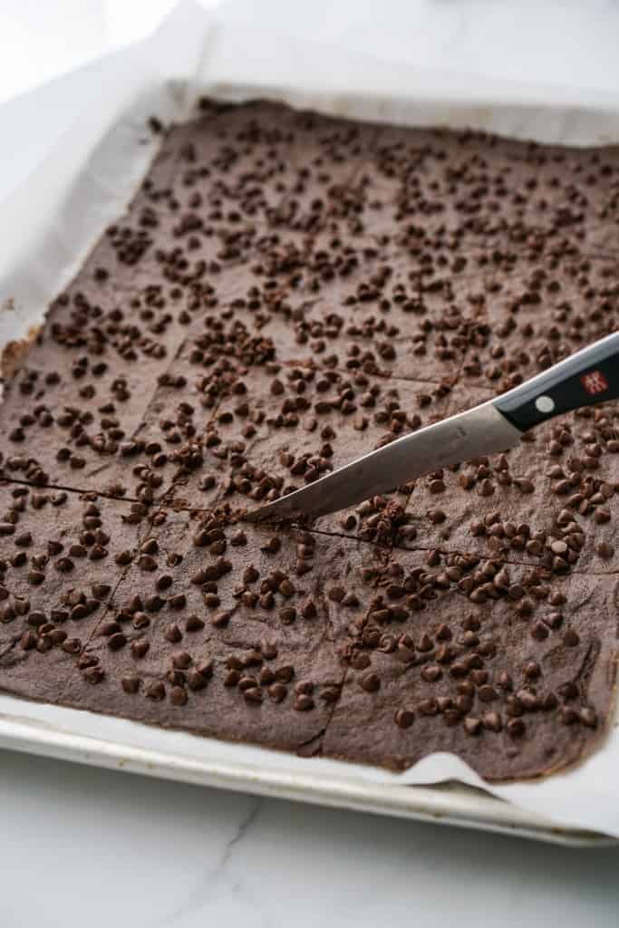 scoring baked chocolate chip brownie crisp with a knife while it is warm