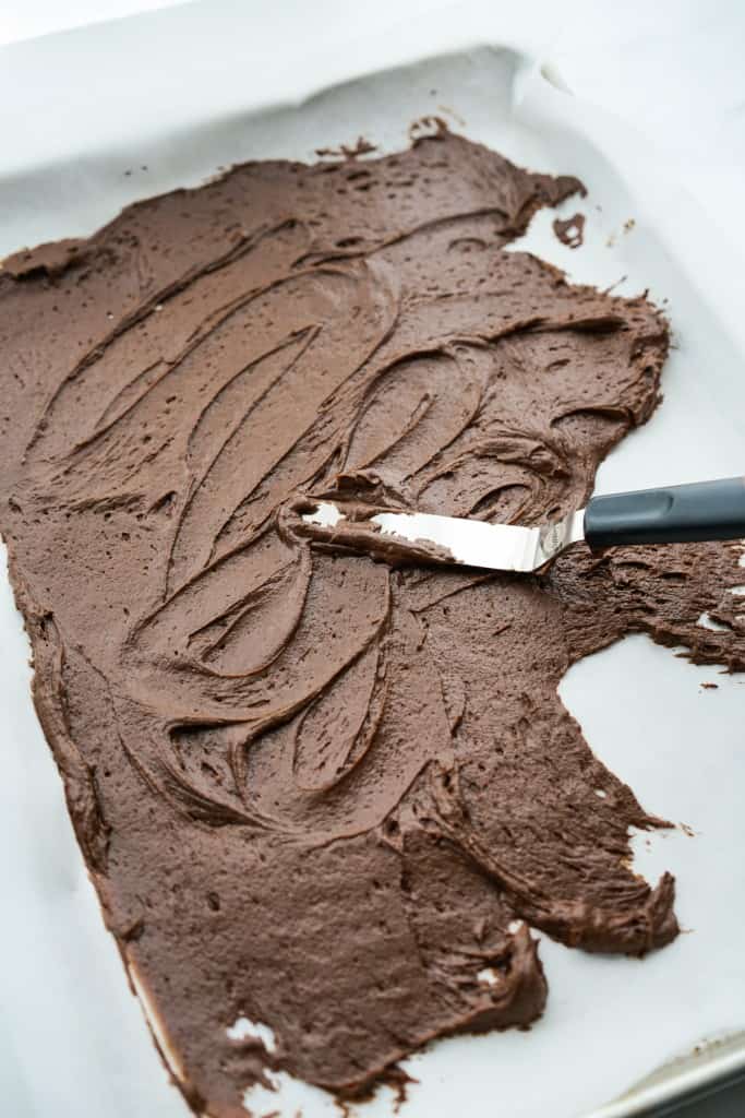 Spreading out brownie brittle mixture on half sheet baking pan lined with parchment paper. 