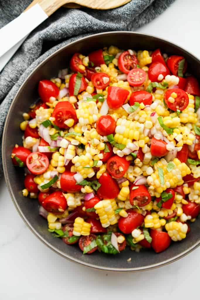 Top down view of a bowl of corn kernels, cherry tomatoes, red onions and fresh basil tossed together.