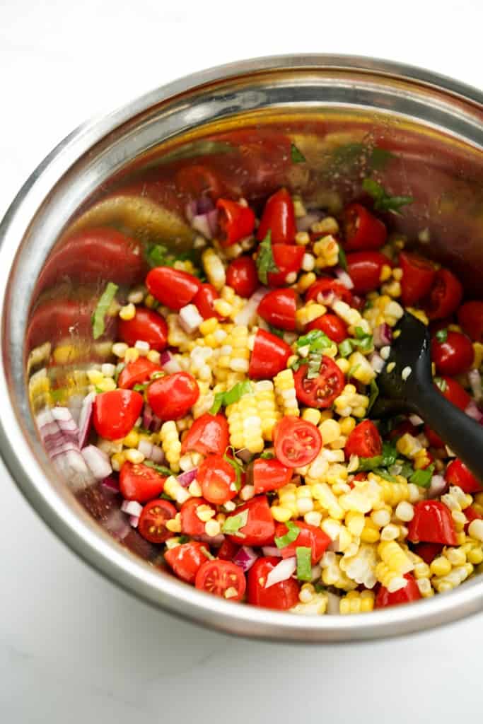 Tossed corn tomato salad in a mixing bowl with a spatula in it