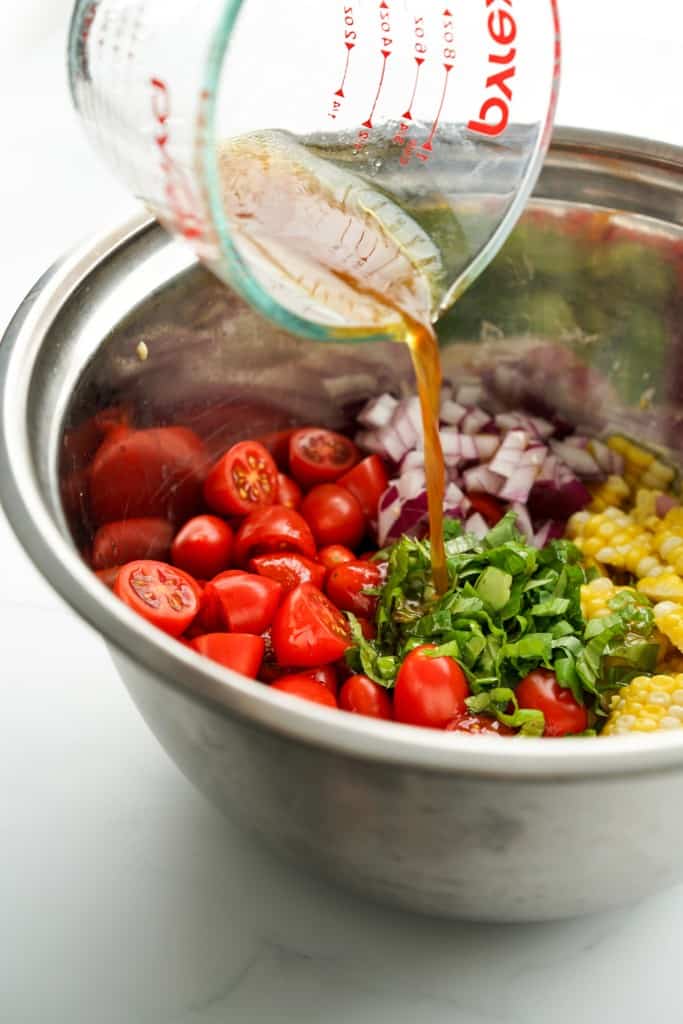 Pouring dressing into corn and tomato mixture in a mixing bowl